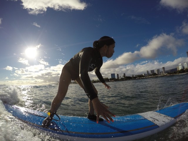 A girl riding a wave with the sun and city skyline as a beautiful backdrop. Provided by Polu Lani Surf.