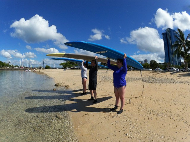 A group of 3, two ladies and a gentleman, with their boards resting on their heads about to start their private surf lesson. Provided by Polu Lani Surf.