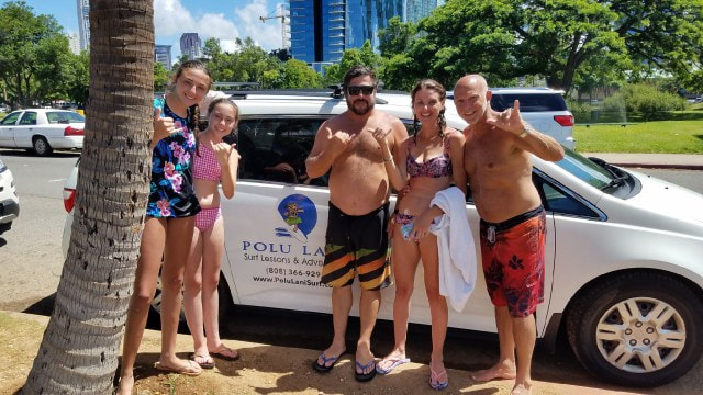 Owner and Instructor, John, with a family of 4 throwing shakas posing in front of the Polu Lani Surf van. Provided by Polu Lani Surf.