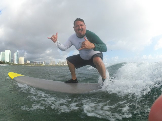 Owner and Instructor, John, of Polu Lani Surf catching a wave throwing a double shaka!
