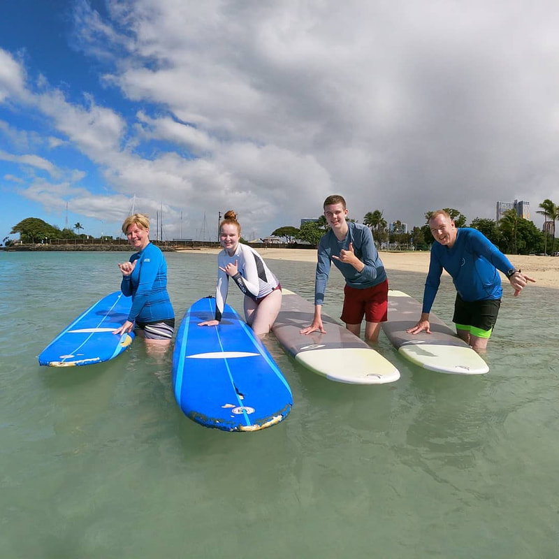 A dad and his 3 children throwing shakas about to start their private surf lesson. Provided by Polu Lani Surf