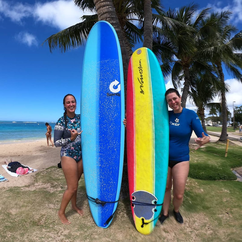 Two young ladies with their boards throwing shakas about to start their private surfing lesson. Provided by Polu Lani Surf