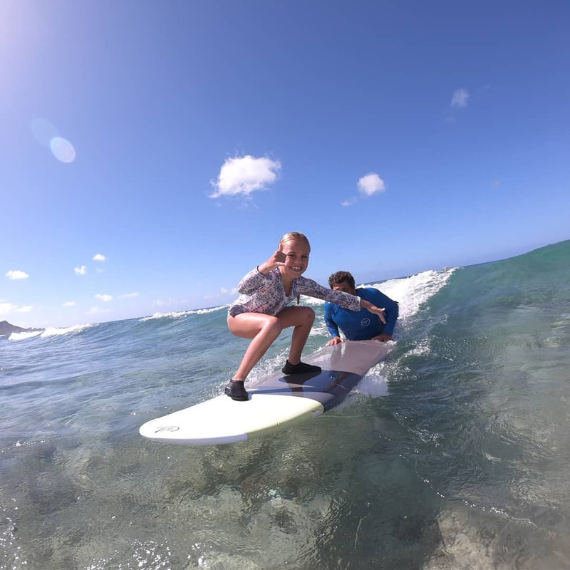 A young girl and instructor / owner, John, catching a wave together, throwing the shaka. Provided by Polu Lani Surf.