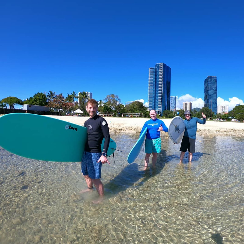 A group of three guys with their boards heading into the water, about to start their private surf lesson. Provided by Polu Lani Surf.