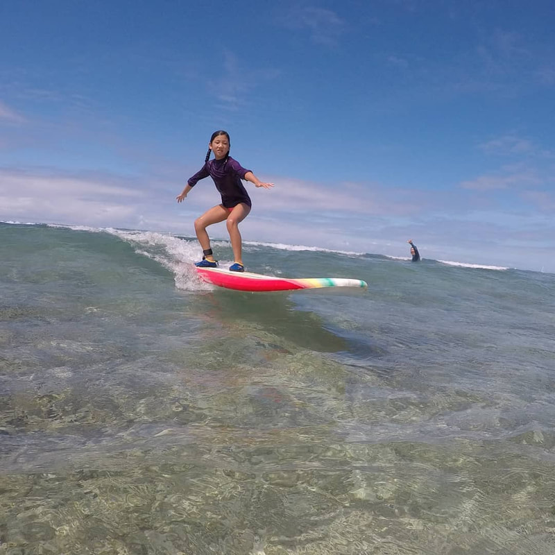 A young girl riding a wave. Provided by Polu Lani Surf.